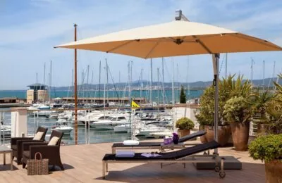 Luxury resort terrace with lounge chairs and umbrella overlooking a marina filled with yachts.