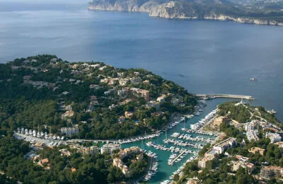 Aerial view of the marina and coastal town of Port d’Andratx in Sant Elm, Mallorca, surrounded by green hills and the sea.