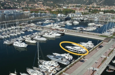 Marina with numerous docked yachts, including a large white yacht highlighted with a yellow circle near the promenade.
