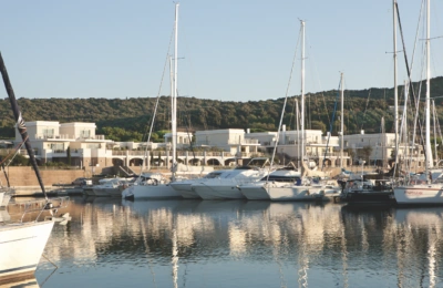 Luxusyachten in einem modernen Yachthafen mit modernen weißen Villen am Wasser und einem bewaldeten Hügel im Hintergrund.