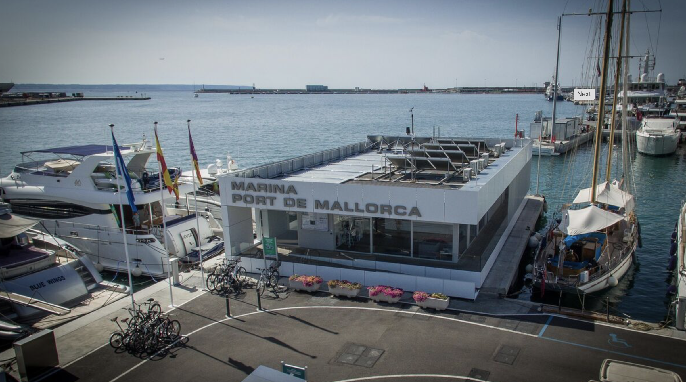 Modern marina office building at Port de Mallorca surrounded by yachts, boats, and dockside bicycles.