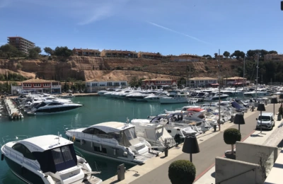 Luxusjachten in einem sonnigen Yachthafen mit roten Dächern und Klippen im Hintergrund.