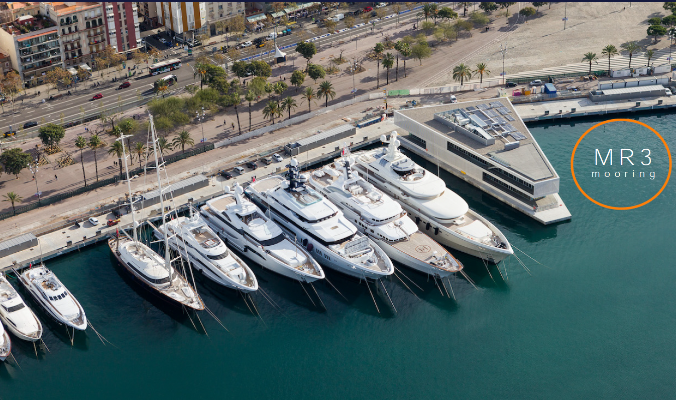 Aerial view of luxury yachts docked at MR3 mooring in a modern marina near a palm-lined promenade.
