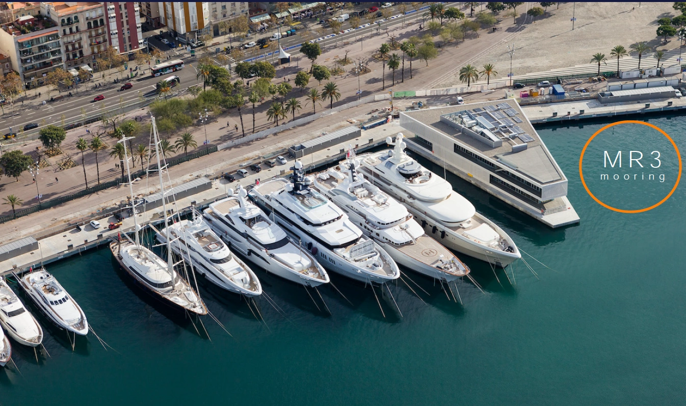 Aerial view of luxury yachts docked at MR3 mooring in a modern marina near a palm-lined promenade.