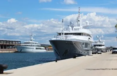 Luxury yacht Siren docked at a marina alongside several other large yachts under a blue sky.