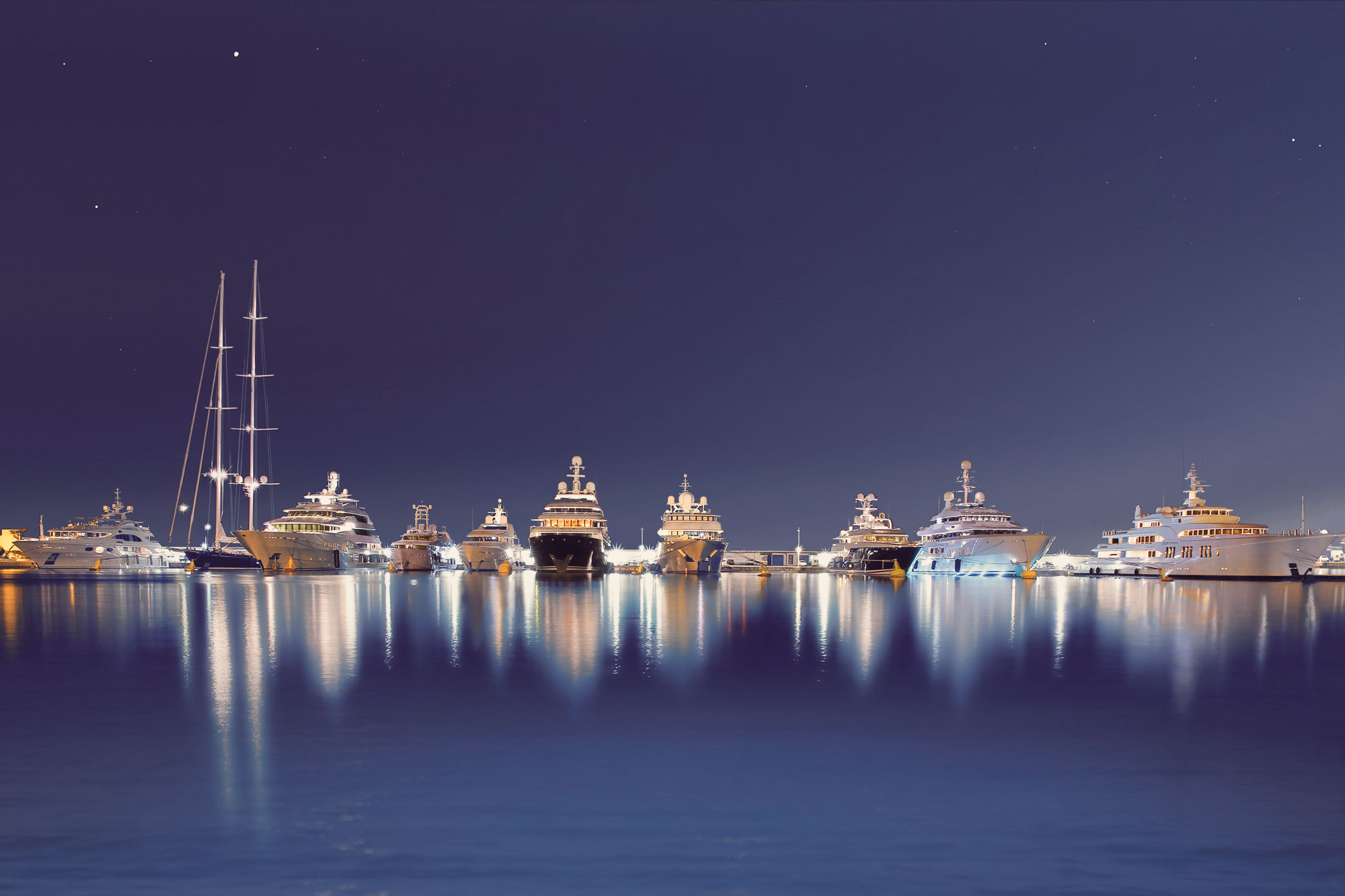 Luxury yachts illuminated at night in Port Vauban, reflecting on the calm water.