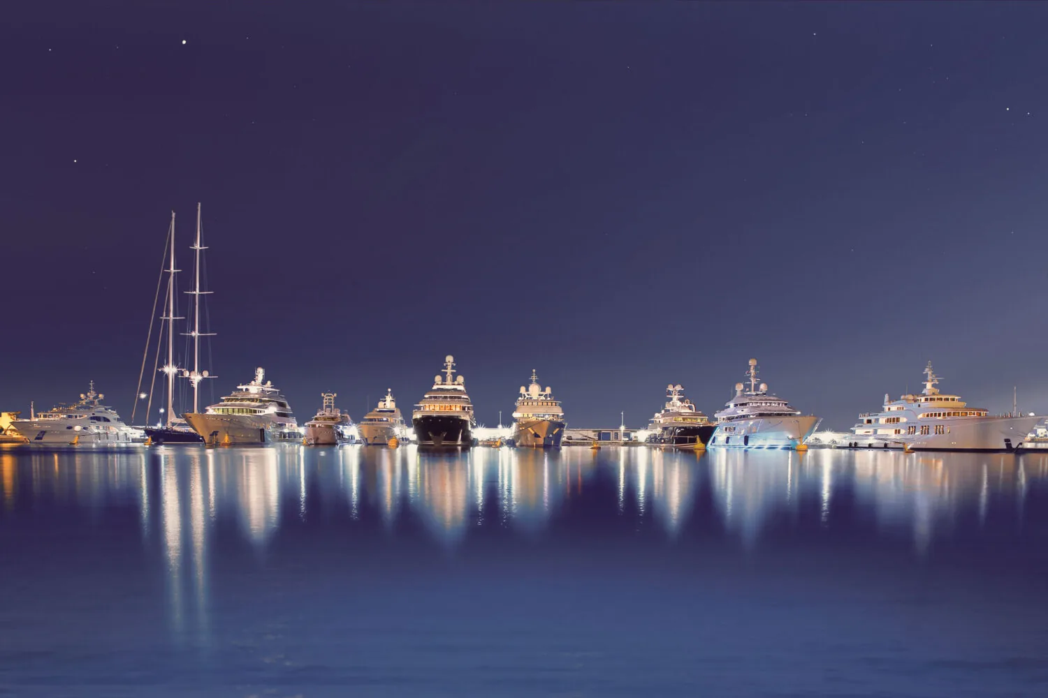 Luxury yachts illuminated at night in Port Vauban, reflecting on the calm water.