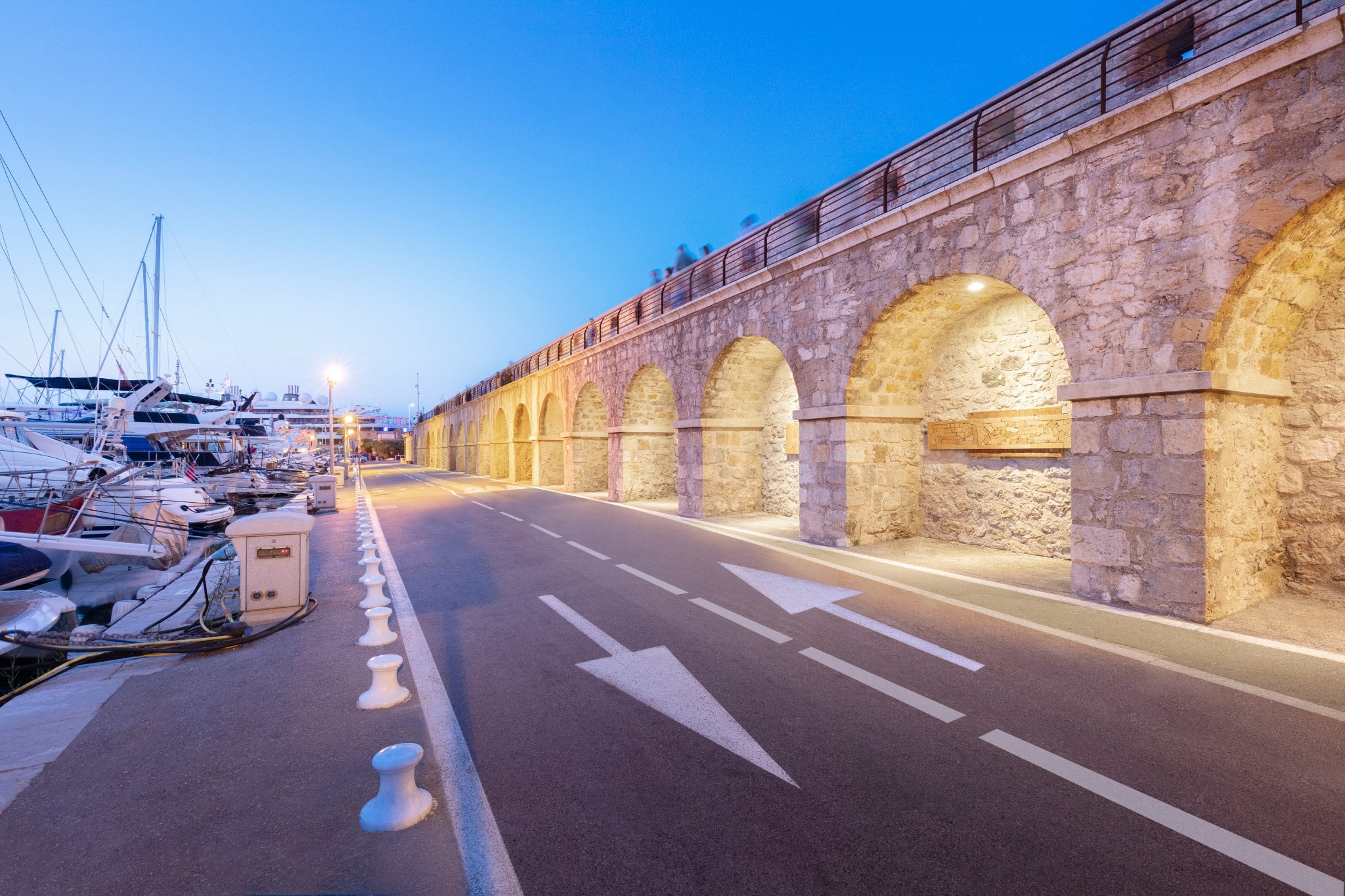 Stone arches of the Vauban 5 promenade beside a marina with yachts at dusk.