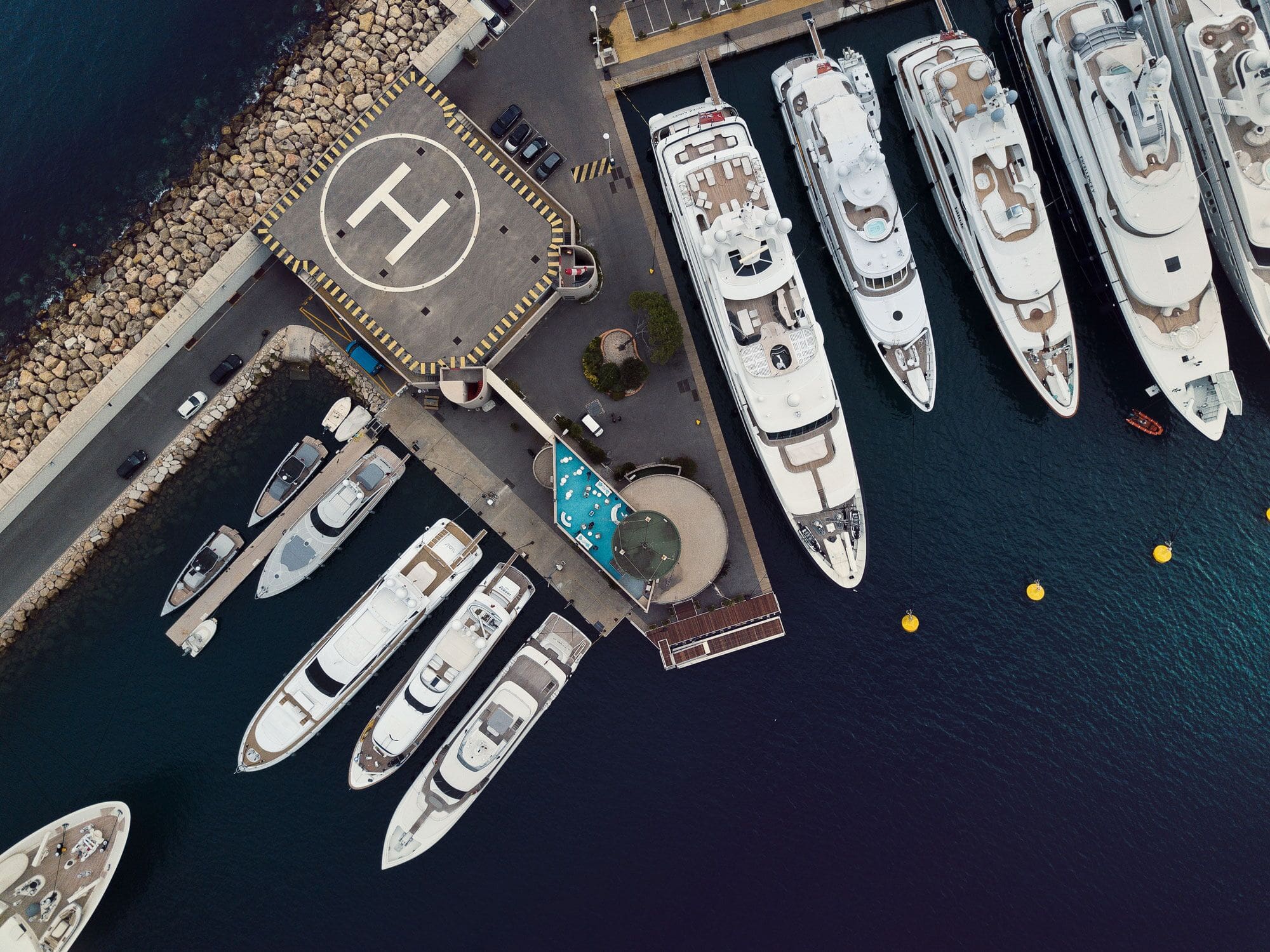 Aerial view of luxury yachts docked at the Vuaban 4 marina next to a helipad and waterfront facilities.