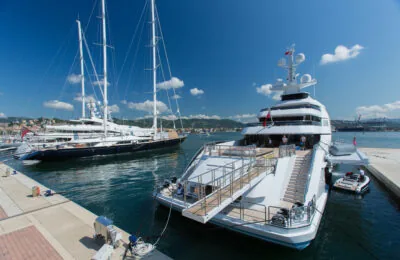 Two large luxury yachts are docked at a harbor under a clear blue sky.