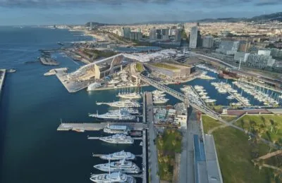 Aerial view of Port Forum in Barcelona with yachts docked and the cityscape in the background.