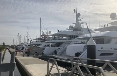 Superyachts moored along a pier at Port Forum marina under a partly cloudy sky.