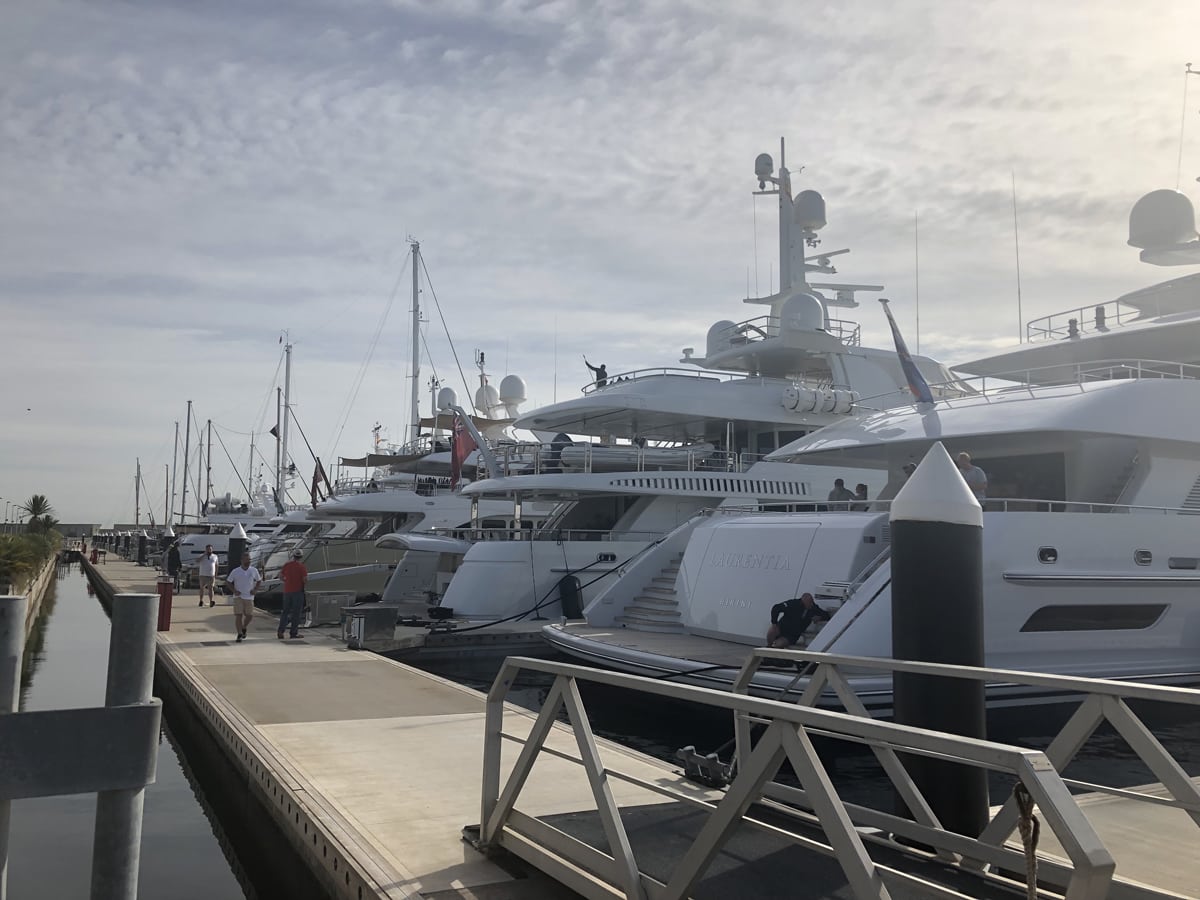 Luxury superyachts moored along the dock at Port Fòrum marina with people walking on the waterfront.