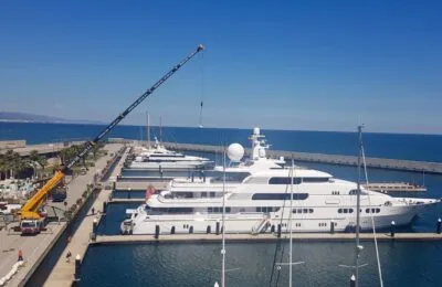 A view of luxury yachts docked at Port Forum Marina with a crane working nearby under a clear blue sky.