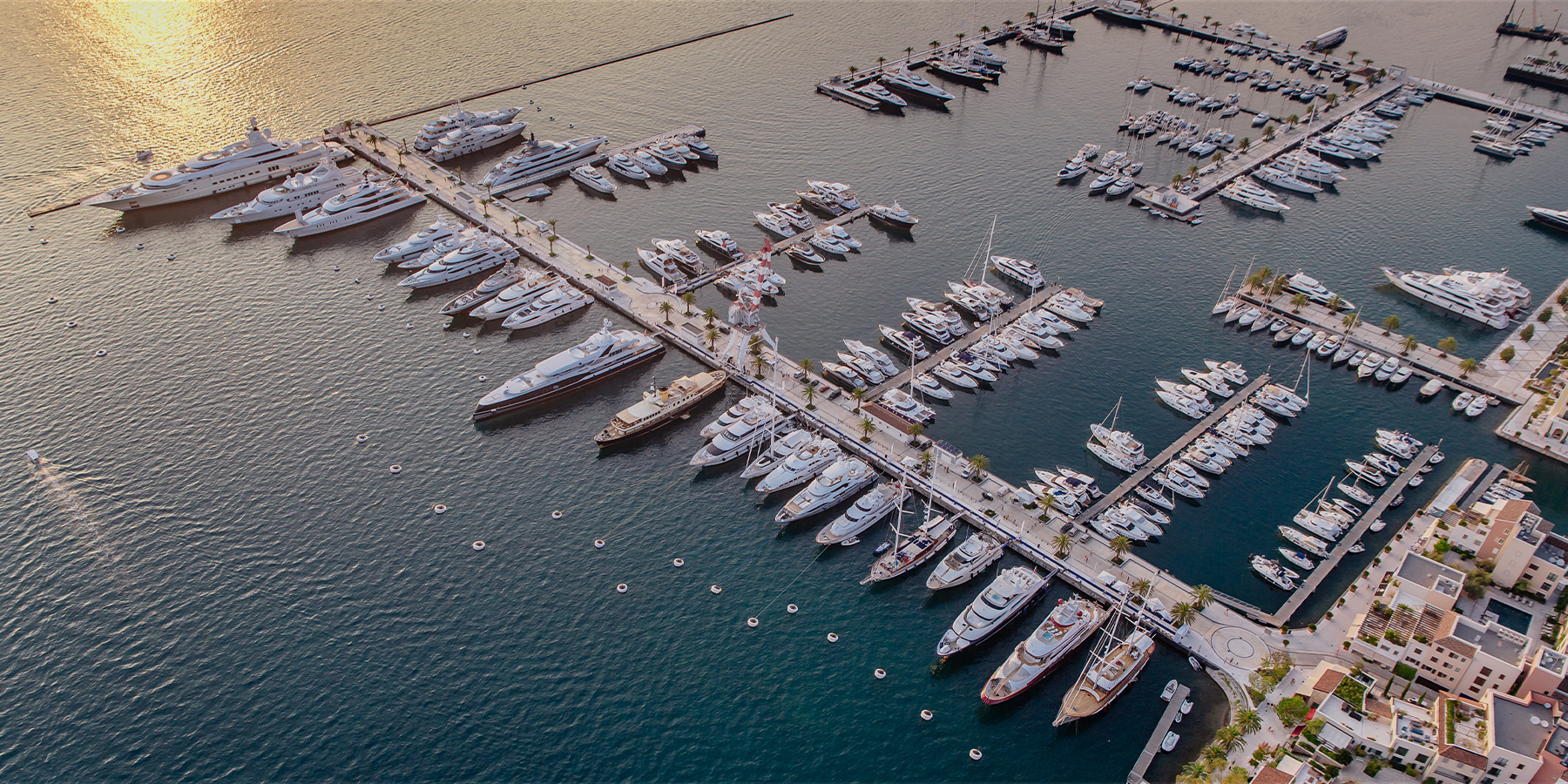 Aerial view of a marina filled with yachts at sunset along a coastal beach.