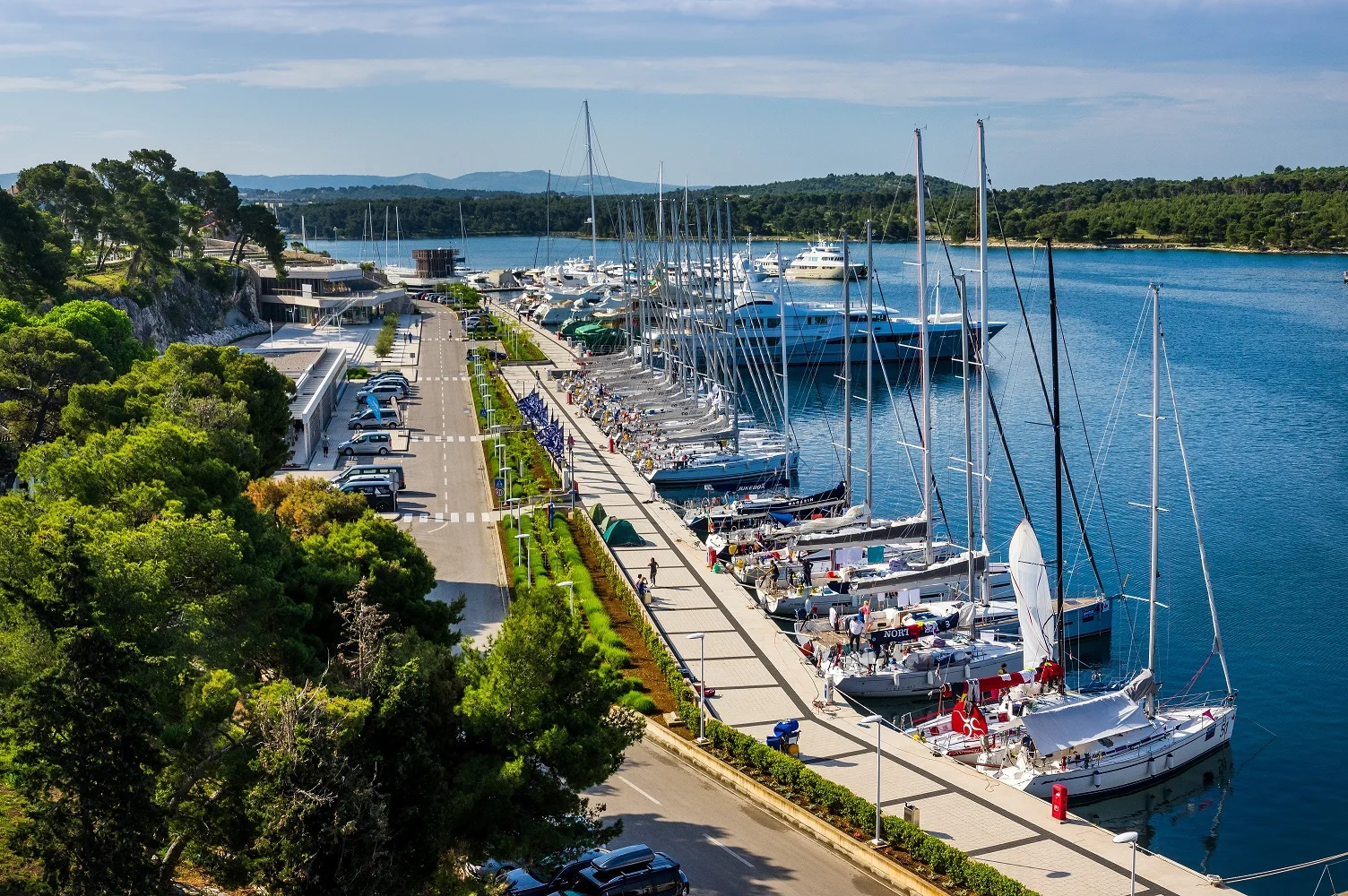 View of Mandalina Marina with docked sailboats and yachts along a scenic waterfront promenade.