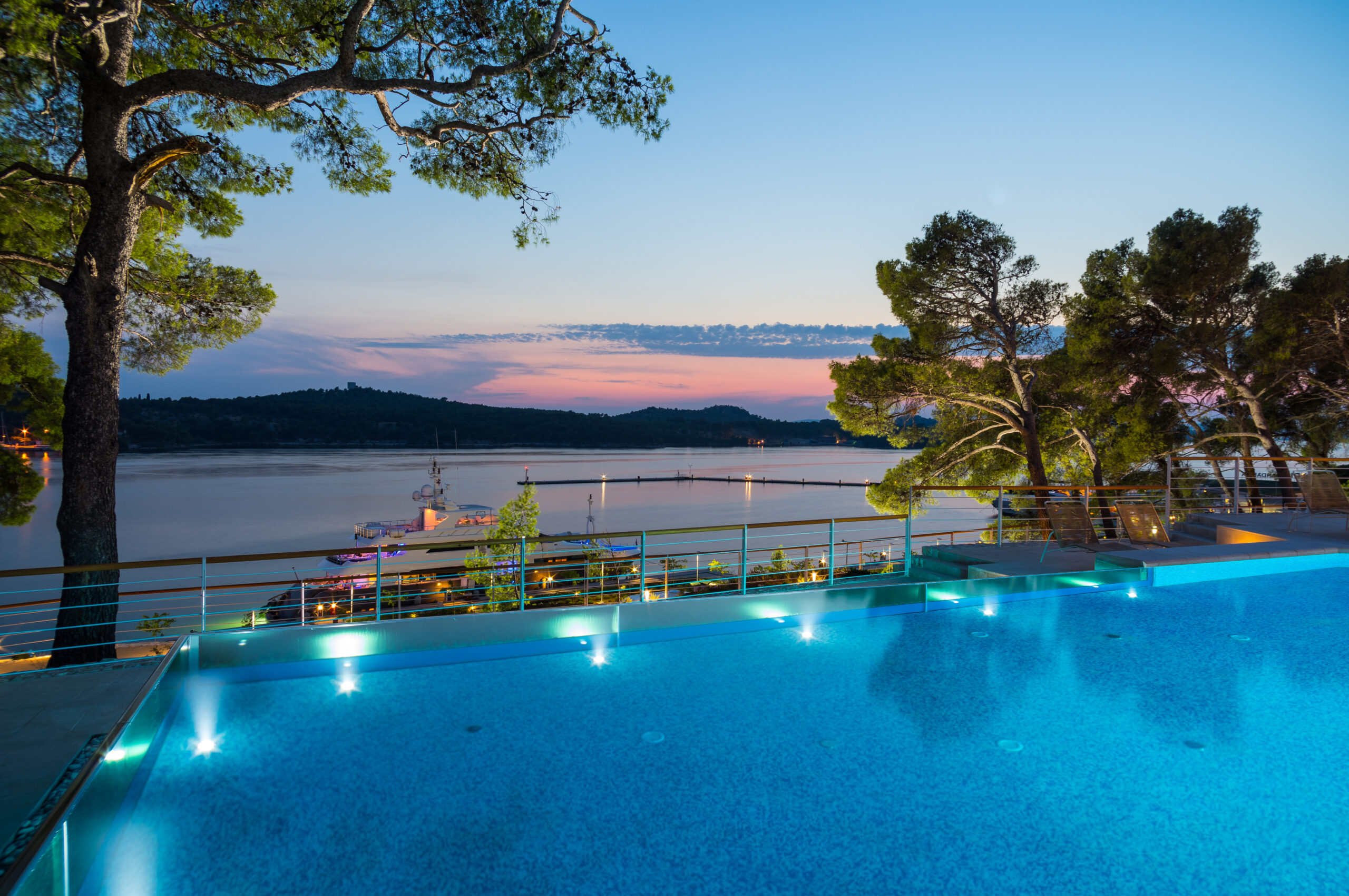 Infinity pool overlooking the Mandalina marina with a serene sunset and forested hills in the background.