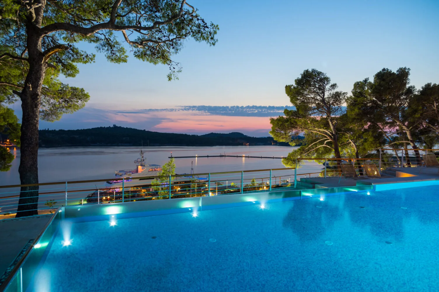 Infinity pool overlooking the Mandalina marina with a serene sunset and forested hills in the background.