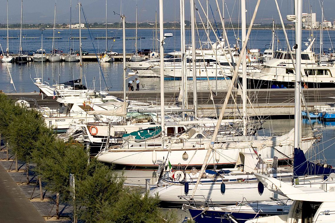 A marina filled with various sailing boats and yachts docked along the waterfront on a sunny day.