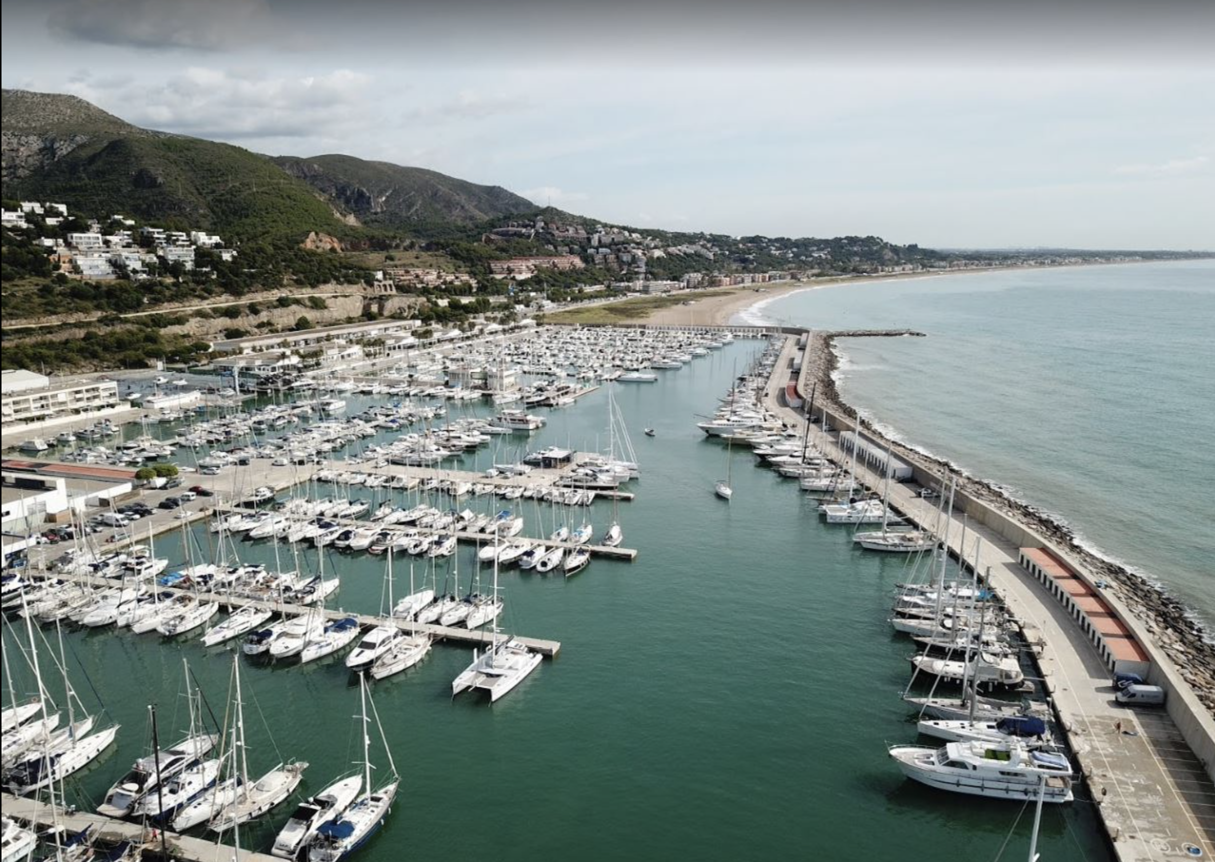 Aerial view of a large marina filled with yachts and sailboats along a scenic coastline.