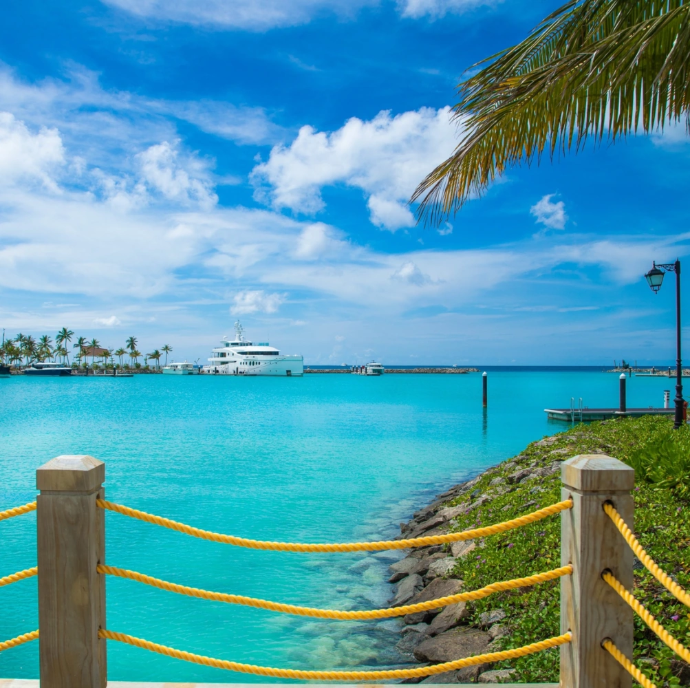 A serene view of a yacht docked at The Yacht Marina by Jalboot, surrounded by turquoise waters and palm trees under a blue sky.