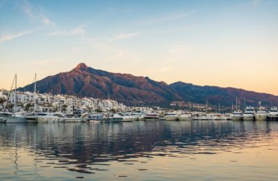 Panoramablick auf den Yachthafen Puerto Banus in Marbella mit angedockten Booten und Bergen im Hintergrund bei Sonnenuntergang.