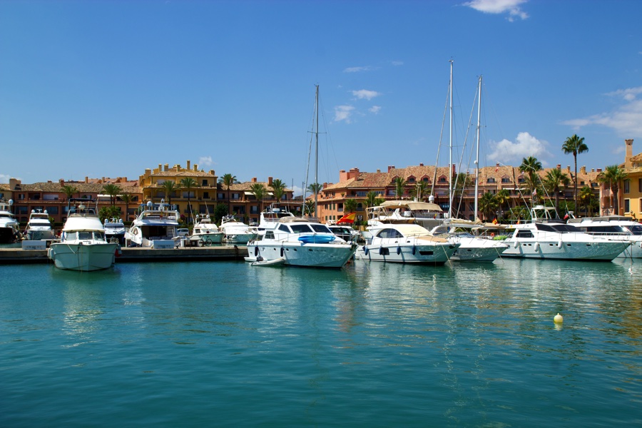 Luxury yachts docked at Puerto Sotogrande marina with colorful waterfront buildings in the background.