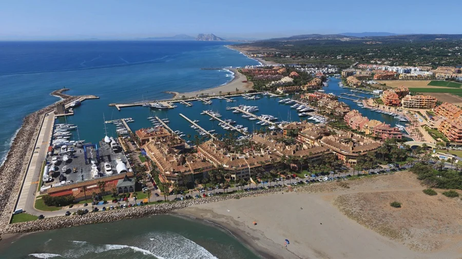 Aerial view of Puerto Sotogrande, showcasing the marina with numerous boats, surrounded by buildings and a beach in the foreground.