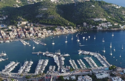 Luftaufnahme von Port Andratx mit zahlreichen vor Anker liegenden Segelbooten, umgeben von üppig grünen Hügeln, wobei der Yachthafen und die Architektur der Küste besonders hervorgehoben werden.